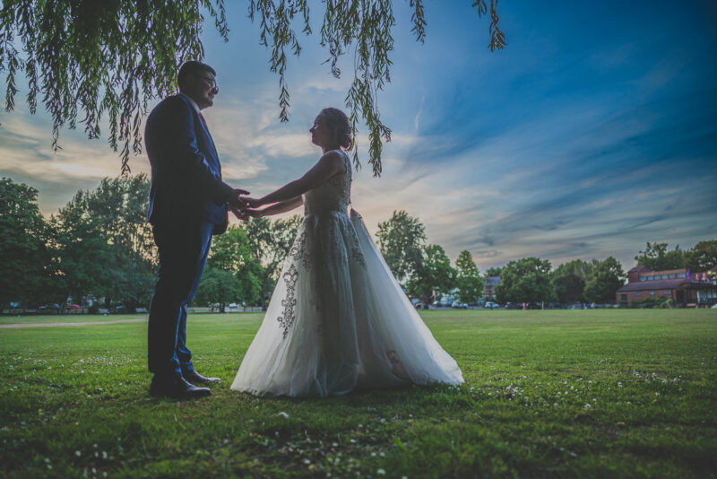 A bride and groom standing under a willow tree at sunset.