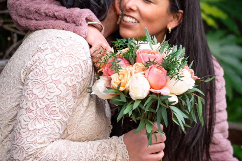 Two women hugging each other while holding a natural bouquet.