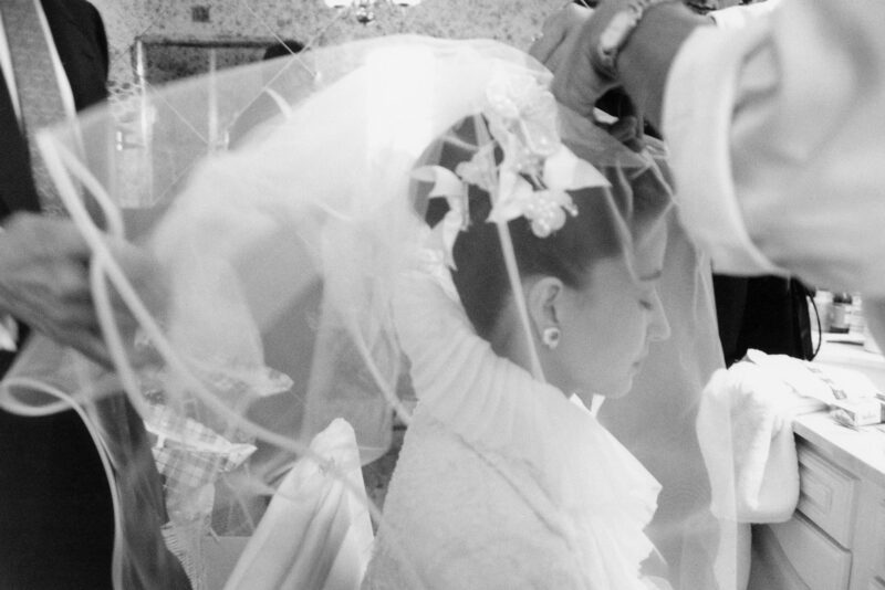 A bride getting her veil on in front of a mirror, captured by a fine art wedding photographer in London.