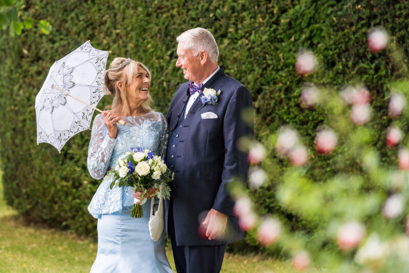 A bride and groom holding an umbrella in a garden.