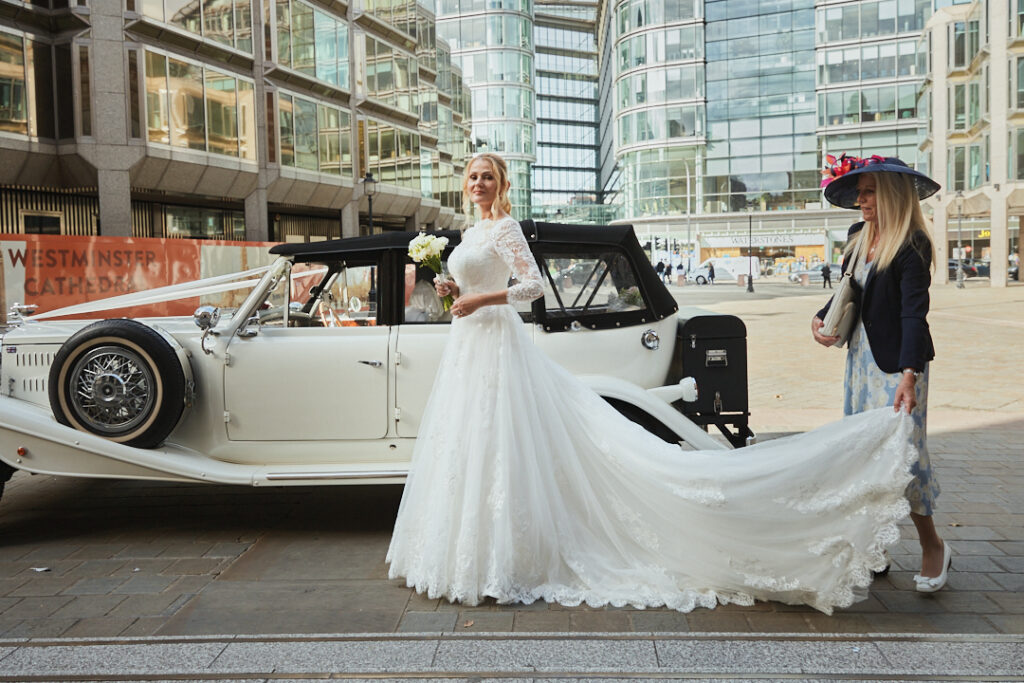 A woman in a wedding dress standing next to a vintage car.