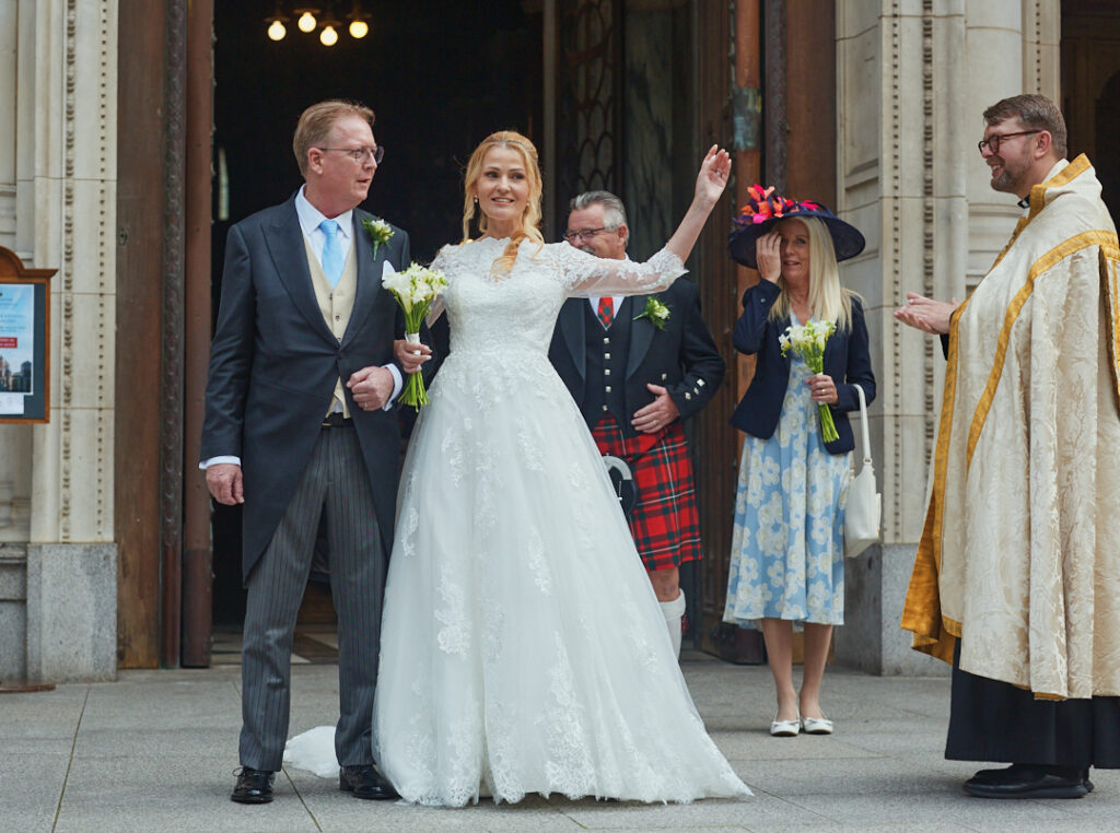 A bride and groom waving as they leave a church.