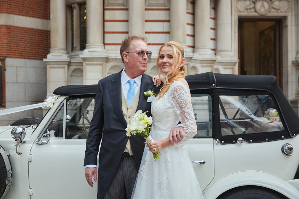 A bride and groom standing next to a vintage car.