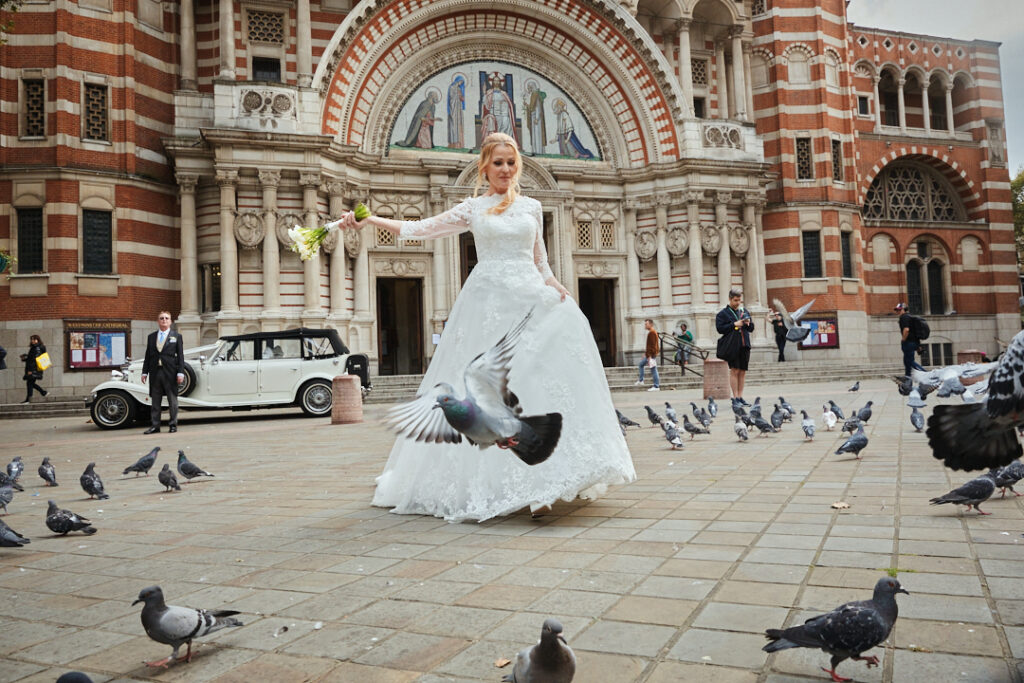 A bride in a wedding dress is surrounded by pigeons.