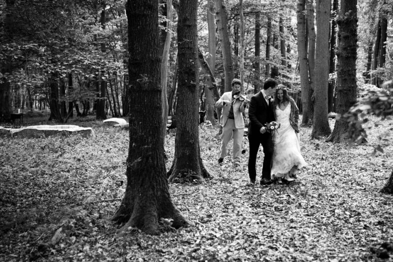 Black and white photo of a bride and groom walking through the woods.
