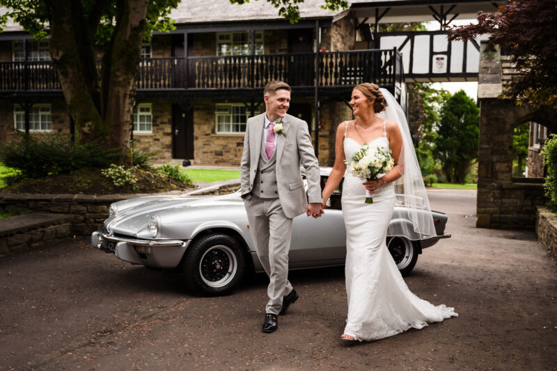 A bride and groom standing next to a classic car.
